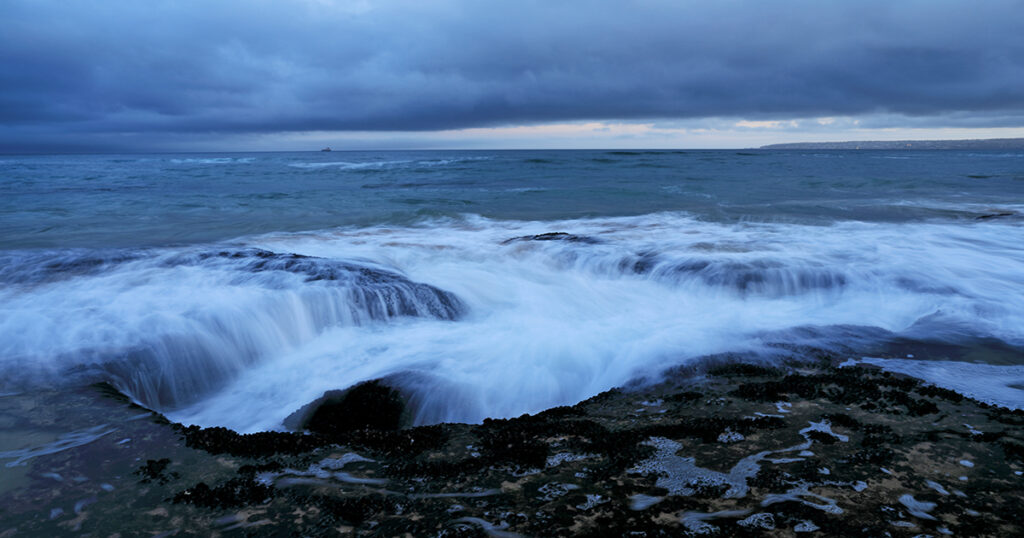 The ocean gently flows over rock and coastline, Mossel Bay.