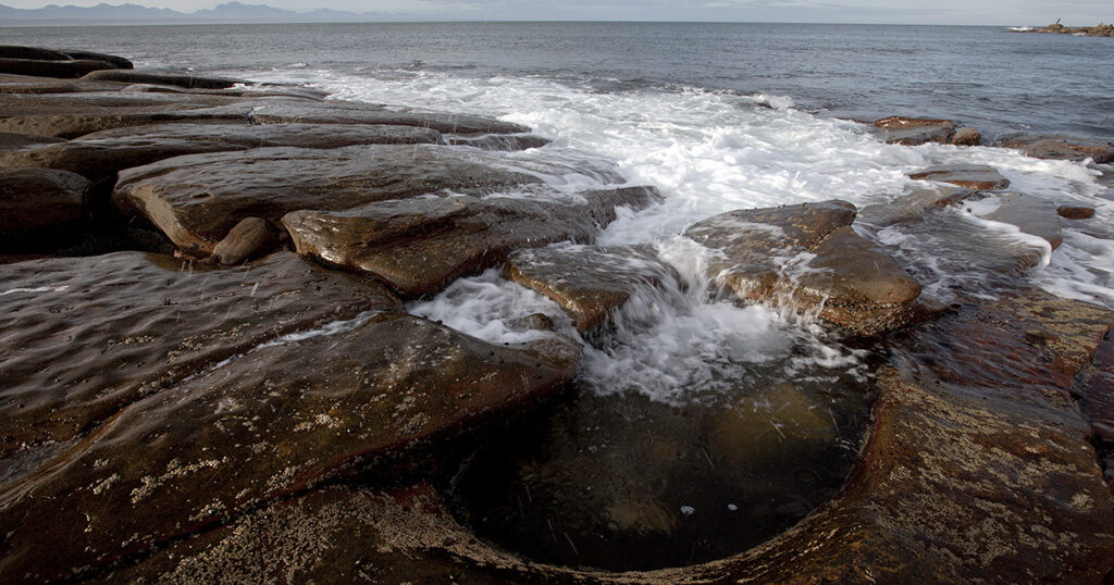 Tidal waters pour into a carved-out rock pool, Mossel Bay.